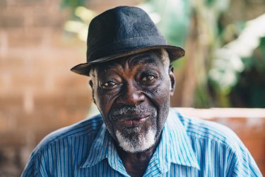 Older black man wearing a hat and blue shirt