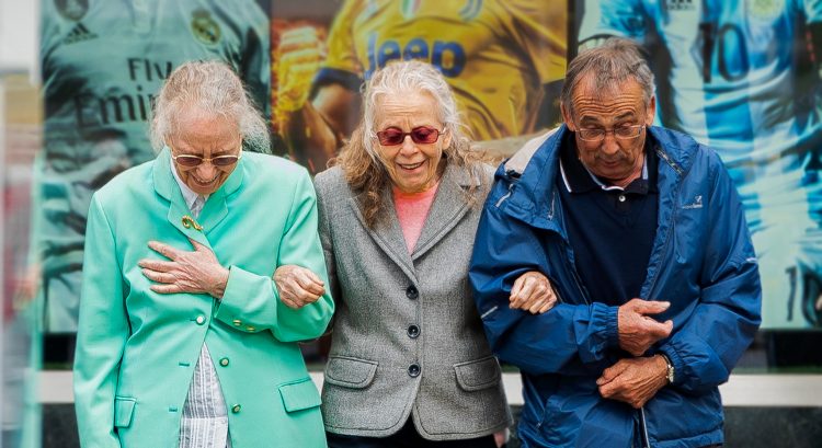 three white, older adults cross the street together; two are woman and one is a man.