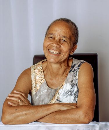 older black woman with short hair and a tank top sitting at a table smiling