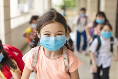 Young girl with braided hair and a mask on running.