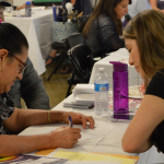 Three people sit at a table during a Brain Health fair to do cognitive testing.