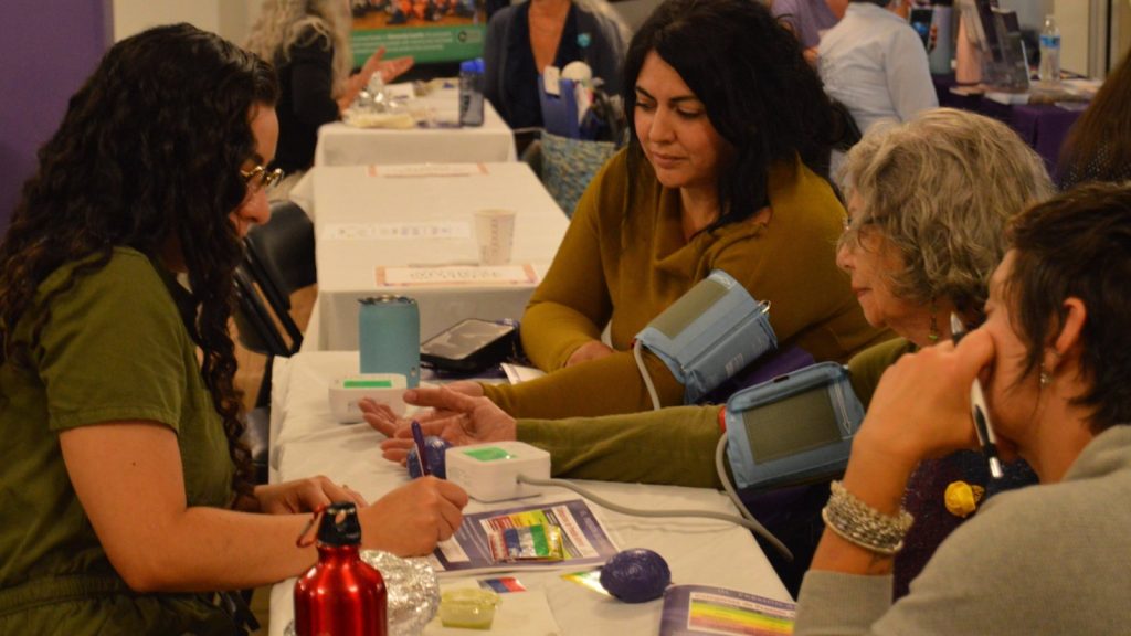 Three people gather around a table to get their blood pressure taken at the Brain Health and Community Resource Fair.