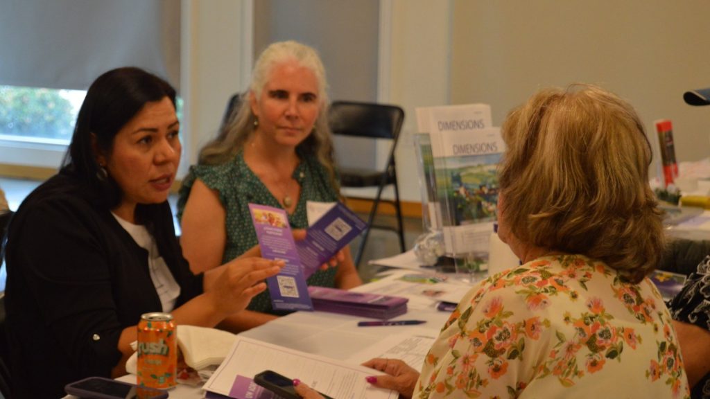 Three people gather around a table to learn about research at the Brain Health and Community Resource Fair.