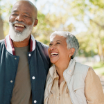 Older adult couple laughs while walking in park.