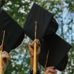 Students hold graduation caps up.